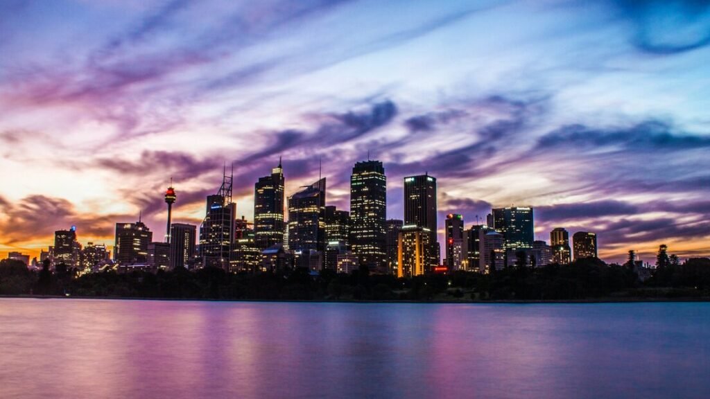 Lighted city buildings near body of water under cloudy sky