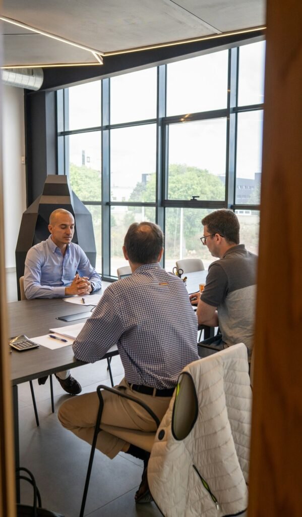 Three people in a meeting at a dark table in a sunlit office