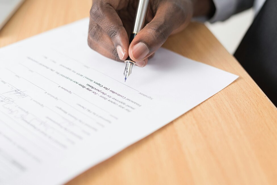 Hands signing a document with a pen on a wooden desk