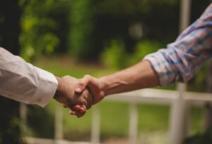 Two people shaking hands in front of a blurred green garden