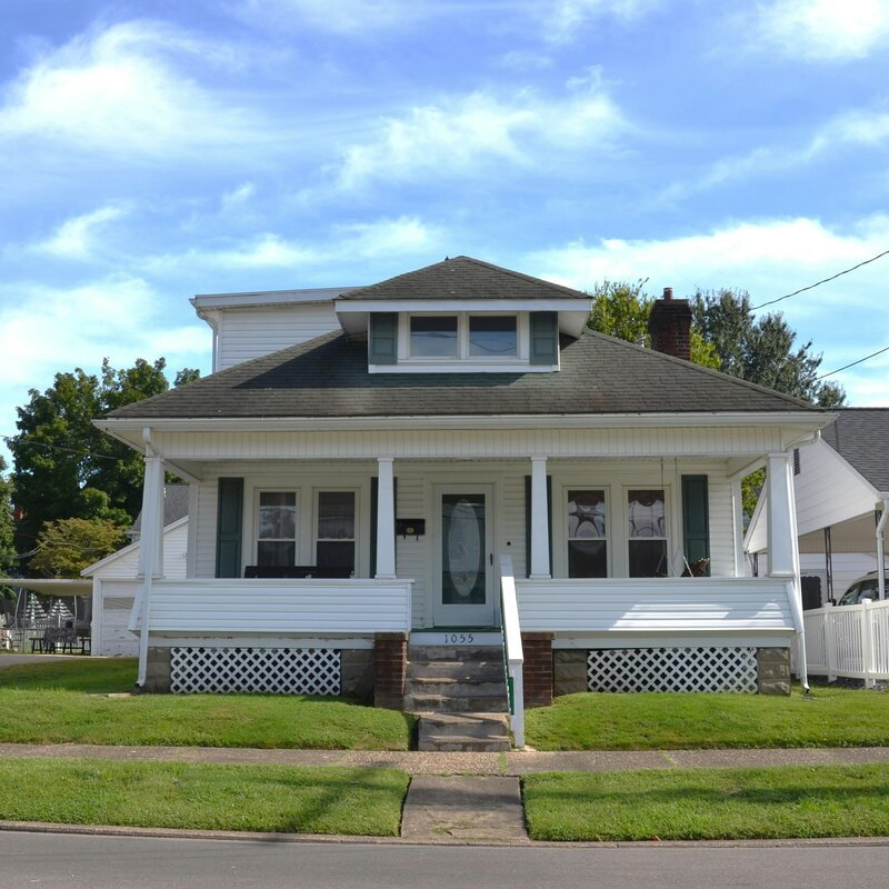 A white house with a front porch and green shutters under a blue sky