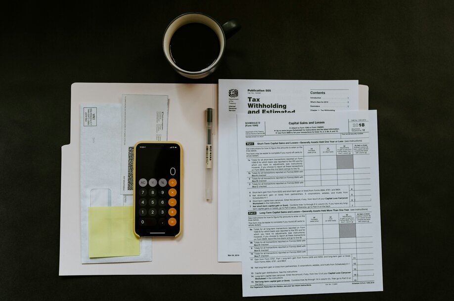 Tax forms, coffee and a phone calculator on a desk seen from above