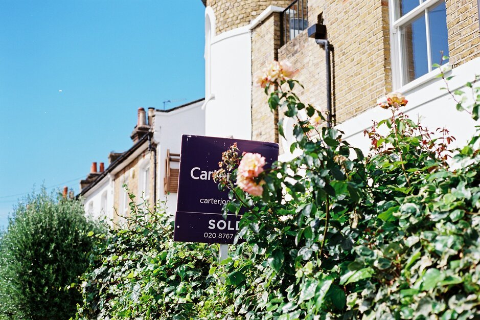A "sold" sign and roses in front of a house