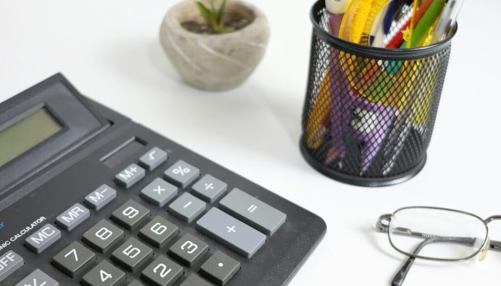 Calculator, glasses, and pens on a white desk