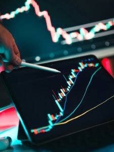 A hand using a stylus to point at a stock market chart on a tablet