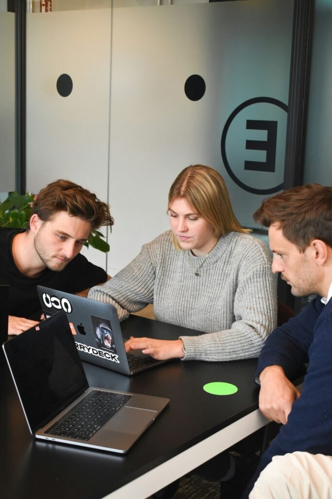 Three people collaborating on a laptop at a black table in an office