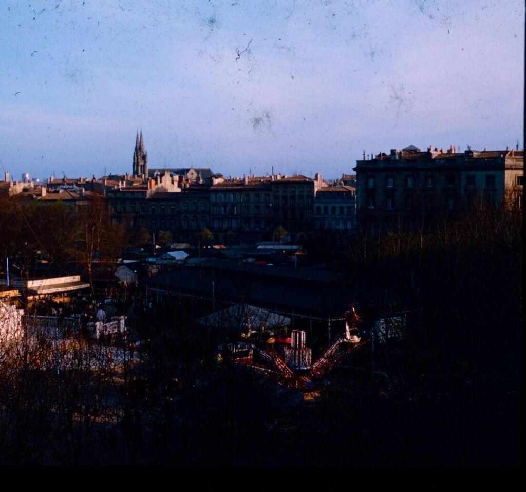 A city skyline with a tall church spire above buildings and a fairground ride in the foreground