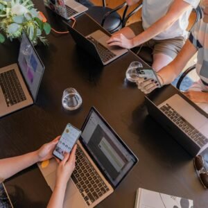 A group of people sitting around a table with laptops