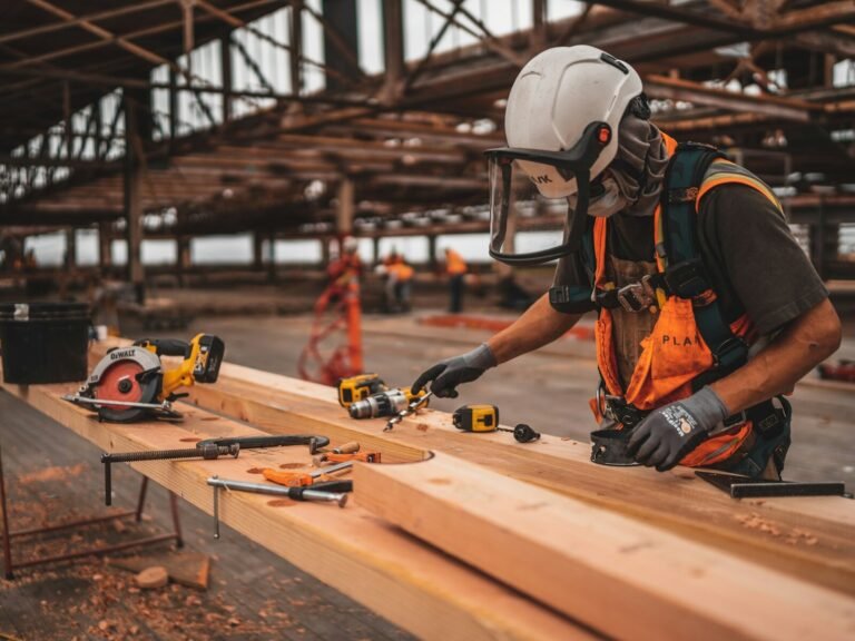 Man in orange and black vest wearing white helmet holding yellow and black power tool