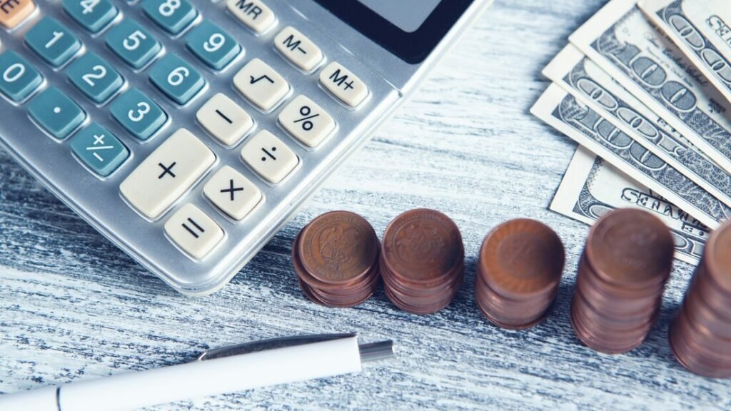 Calculator and stacks of coins on a desk with a pen