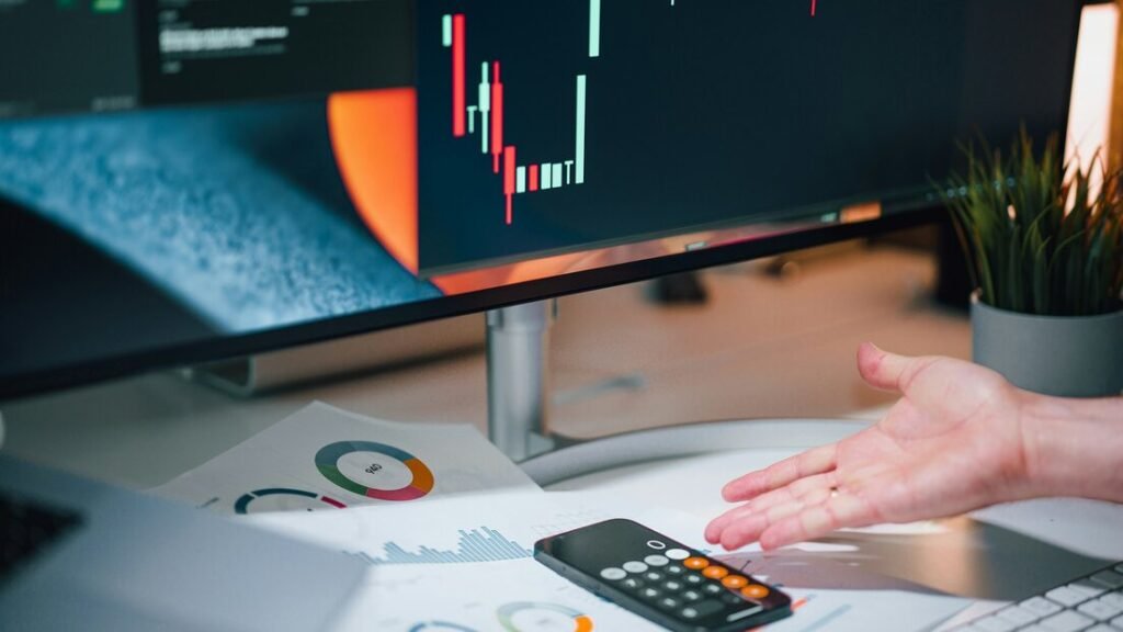 Hand resting on desk with financial charts, a notebook and a calculator