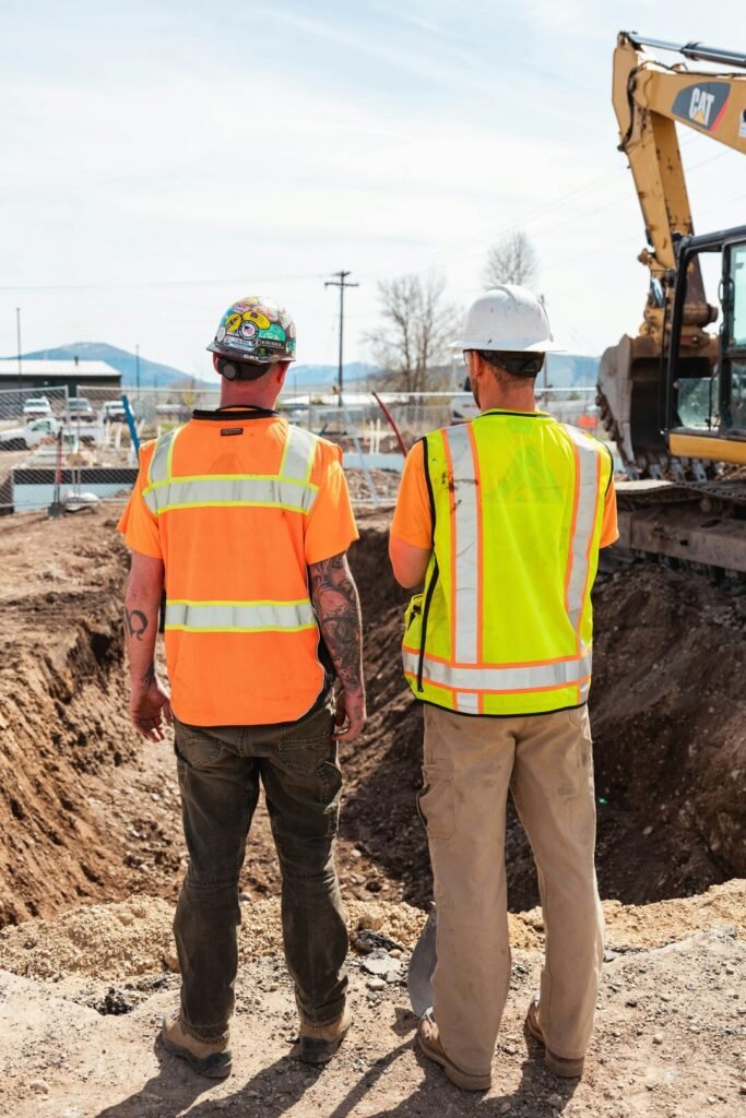 Two construction workers in safety vests looking over a building site