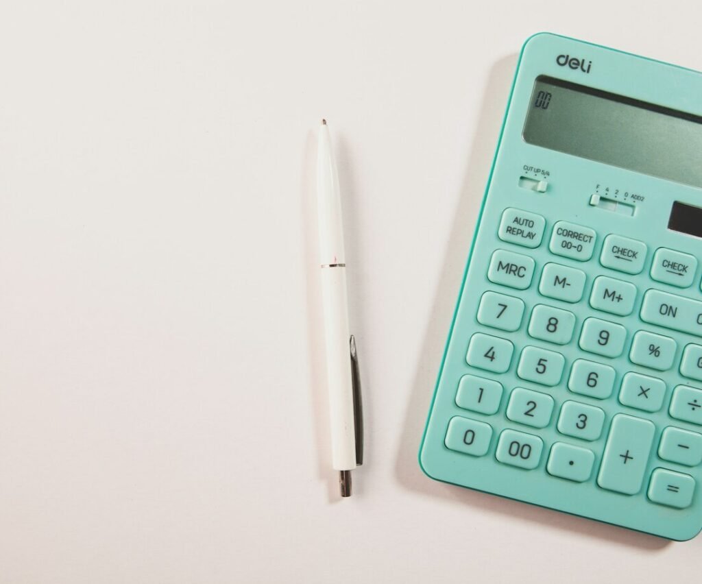 A teal calculator and white pen on a white surface