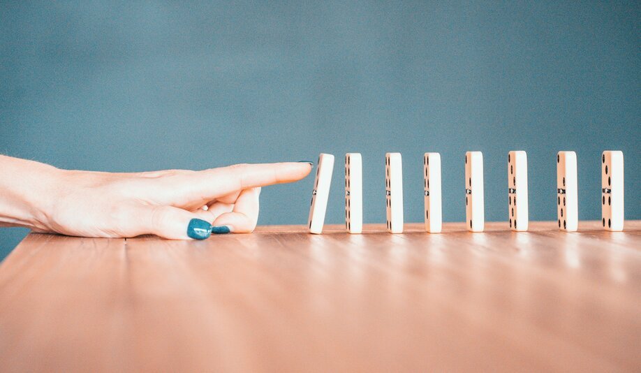Hand pushing a row of standing dominoes, illustrating risk