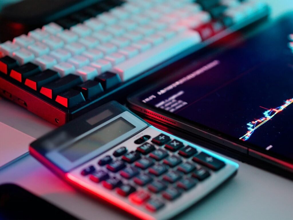 A mechanical keyboard, a calculator, and a tablet displaying a stock market graph