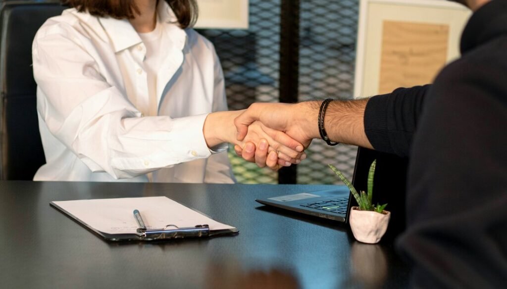 A man and a woman shaking hands in front of a laptop