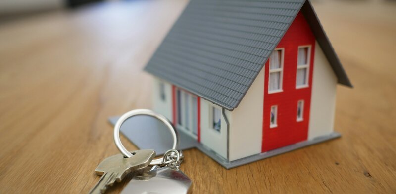 Small model house and keys on a wooden table, representing rental property