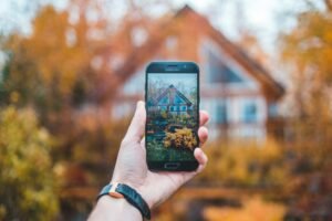 Hand holding a smartphone showing a house, with the same house in the background