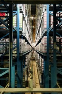 Tall blue metal shelving units filled with stacked boxes in a warehouse aisle
