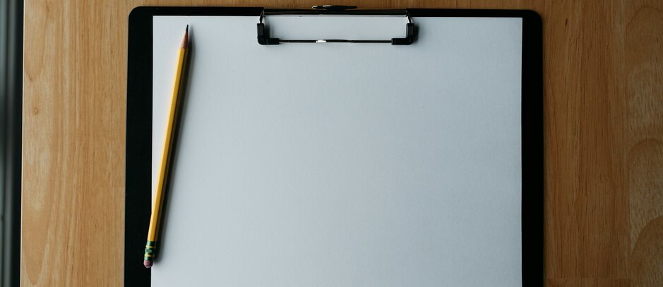 Clipboard, pencil, and pen on a wooden surface